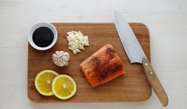 Piece of fresh salmon on a cutting board with lemon, garlic, soy sauce and a knife. Omega-3's during pregnancy.