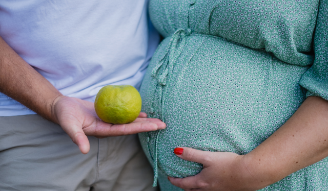 pregnant woman's belly in green dress standing with partner holding a green apple for changes in digestion during pregnancy